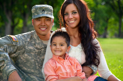 Young Asian-American military service member in desert camouflage fatigues sitting with his wife and young son.